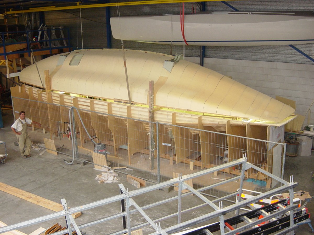 Starboard main hull half fixed in the form frames while the port half is lowered in from above to join into a complete main hull